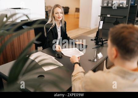 Rückansicht einer Führungskraft, die mit einem männlichen Kollegen über geschäftliche Aufgaben spricht und Dokumente am Tisch im Büro überreicht. Stockfoto