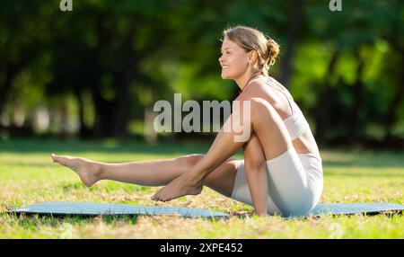 Sportliches Mädchen, das einen Arm ausbalanciert, Elephant Trunk-Pose im Sommerpark Stockfoto