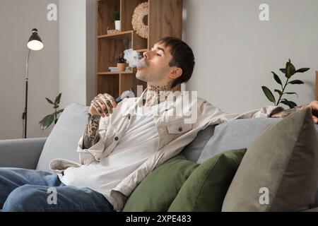 Junger Mann, der zu Hause elektronische Einwegzigarette raucht Stockfoto