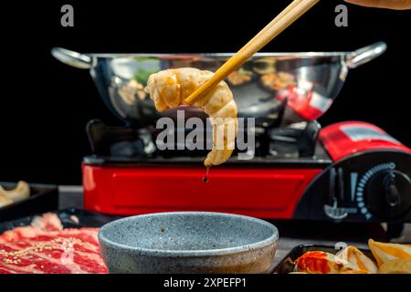 Eine Person kocht Essen mit Stäbchen in einem roten Topf. Die Szene ist eine Person, die eine Mahlzeit genießt Stockfoto