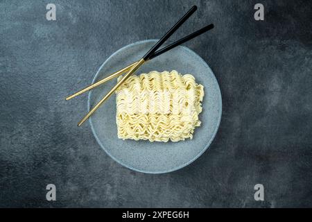 Ein Teller mit Instant-Nudeln mit Essstäbchen darauf. Die Platte befindet sich auf einer grauen Oberfläche. Die Instant-Nudeln sind lang und dünn Stockfoto