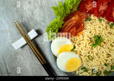 Eine Schüssel mit Instantnudeln mit Eiern und Tomaten. Die Schüssel steht auf einem Tisch mit Stäbchen daneben Stockfoto