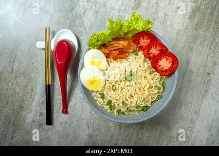 Eine Schüssel mit Instantnudeln mit Eiern und Tomaten. Die Schüssel steht auf einem Tisch mit Stäbchen und einem Löffel Stockfoto