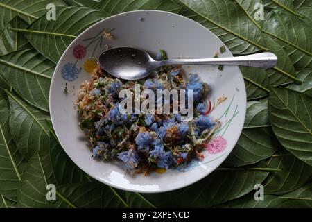 Nahaufnahme von leckerem Kerabu-Reis auf Teller auf grünen verstreuten Blättern. Auch bekannt als khao Yam in Thailand. Stockfoto