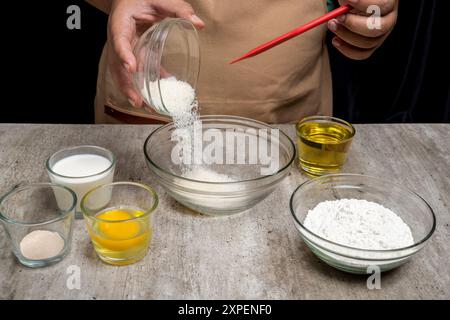 Eine Person macht einen Kuchen und hat eine Schüssel Zucker vor sich. Auf dem Tisch stehen noch andere Schüsseln und Tassen, darunter eine mit Mehl und eine andere Stockfoto