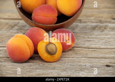 Ein Haufen reifer Aprikosen und eine in zwei Hälften geschnitten, um den saftigen Innenraum, rustikalen Holztisch zu präsentieren Stockfoto