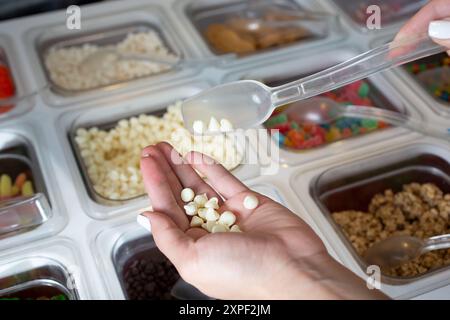 Ein Blick auf eine Hand, die über einer Theke voller verschiedener Beläge steht, die in einem lokalen Tiefkühljoghurt-Restaurant zu sehen ist. Stockfoto