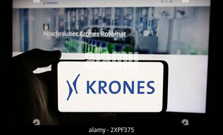Person mit Handy mit Logo des deutschen Ingenieurunternehmens Krones AG vor der Business-Webseite. Schwerpunkt auf dem Display des Telefons. Stockfoto