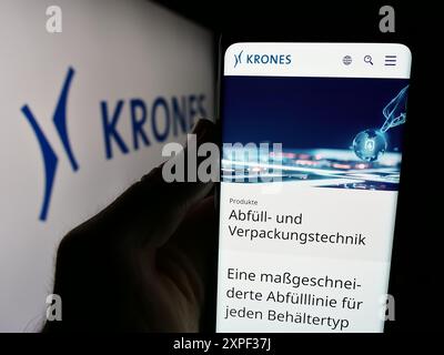 Person mit Handy mit Webseite des deutschen Ingenieurunternehmens Krones AG vor dem Firmenlogo. Konzentrieren Sie sich auf die Mitte des Telefondisplays. Stockfoto