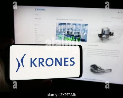 Person mit Smartphone mit Logo des deutschen Ingenieurunternehmens Krones AG vor der Website. Schwerpunkt auf dem Display des Telefons. Stockfoto