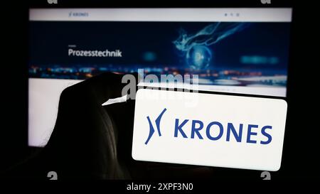 Person mit Mobiltelefon mit Logo des deutschen Ingenieurunternehmens Krones AG vor der Business-Webseite. Schwerpunkt auf dem Display des Telefons. Stockfoto