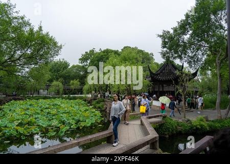 Suzhou, China - 11. Juni 2024 : Eine Steinbrücke überquert einen Teich mit Lotusblättern. Besucher spazieren entlang der Brücke und durch ein klassisches Chinesisch Stockfoto