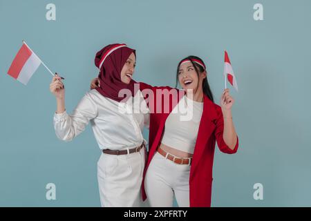 Zwei wunderschöne indonesische Frauen, die eine Minifahne halten, während sie sich mit einem Lächeln anschauen. Indonesien Unabhängigkeitstag Konzept. Stockfoto