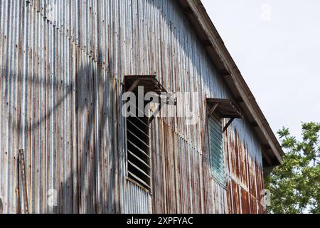 Blechhaus mit Fenstern verrostet und beschädigt. Das Äußere eines Wohnhauses ist verrostet und beschädigt. Wellblechhaus Stockfoto