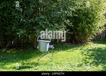 Plastikeimer hängt an einem Sommermorgen in einem sonnendurchfluteten städtischen Garten auf einem Metallstuhl Stockfoto