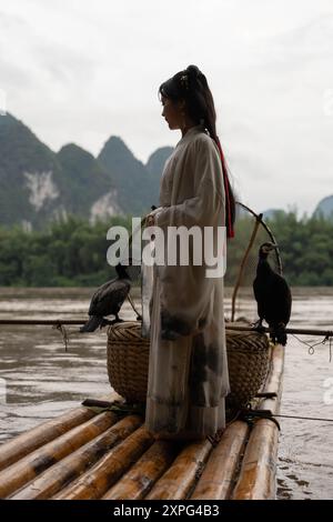 Chinesisches Hanfu-Mädchen, das ihre Haare repariert, während es auf einem Bambusfloß am Fluss Li, Xingping, steht Stockfoto