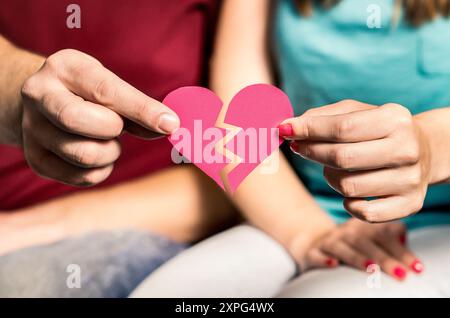 Scheidung, Trennung oder Trennung. Zerrissenes Papierherz in den Händen eines Paares. Suche nach Match und Liebe. Betrügen, Untreue, Verrat oder Vertrauensprobleme. Stockfoto
