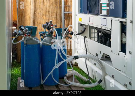 Gasflaschen, die mit Geräten in einem Hinterhof verbunden sind, mit hellem Sonnenlicht, das die Szene beleuchtet, und Grün im Hintergrund. Stockfoto