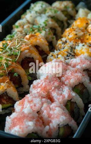 Köstliche Sushi-Brötchen nebeneinander in einem schwarzen Tablett. Nahaufnahme mit selektivem Fokus und geringer Schärfentiefe. Stockfoto