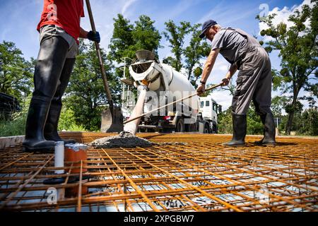 Arbeiter, der Beton aus einem Mischer auf Rebar Framework verteilt Stockfoto