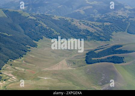 Luftlandschaft, von einem Segelflugzeug, mit einem Segelflugzeug im Flug über den grünen Hängen von Castelluccio, von oben in hellem Sommerlicht aufgenommen, A Stockfoto