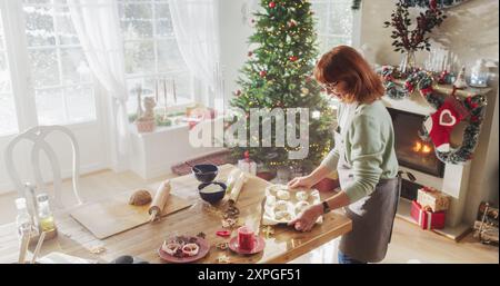 Porträt einer Senior-Frau, die Zimtbrötchen zu Weihnachten zu Hause macht. Fröhliche Hausfrau und Großmutter, die Gebäck für den Urlaub mit Familie und Freunden teilen Stockfoto