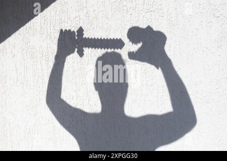 Die Silhouette des Mannes vor einer weißen Wand mit einem Dinosaurier in der einen Hand und einem Schwert in der anderen. Interessante kontrastierende Schatten an der Wand. Ideen für SHA Stockfoto