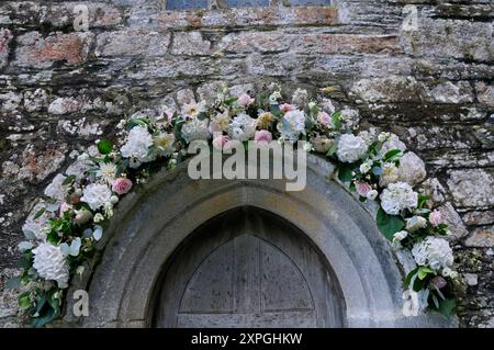 Eine Mischung aus Rosen, Hortensien und Dahlien um den Steinbogen einer hölzernen Kirchentür als Hochzeitsblumen Dekoration, St. Just in Roseland, Cornwall, Großbritannien Stockfoto