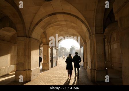 Ein elegantes junges Paar, das durch den sonnigen, gewölbten Gang des Horse Guards-Gebäudes von Whitehall zum Paradegelände spaziert. London, England Großbritannien Stockfoto