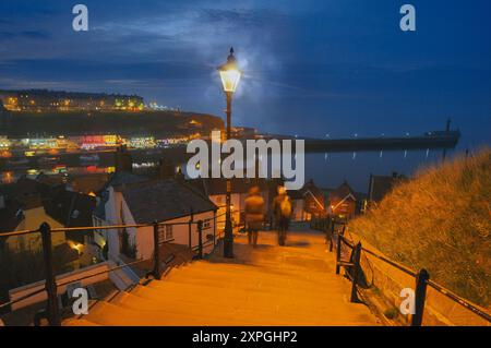 Menschen gehen die berühmten 199 Stufen bei Nacht hinunter in die Altstadt von Whitby mit Blick auf den Fluss esk, Hafen und Pier, North Yorkshire Coast, England, Großbritannien Stockfoto