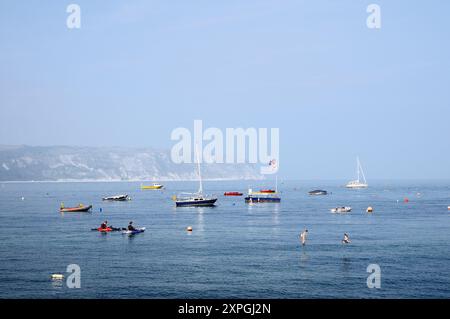 Boote, die an einem sonnigen, trüben Sommermorgen in Swanage Bay vor Anker liegen, mit Kreidefelsen von Ballard Down und Ballard Point dahinter, Jurassic Coast, Dorset England, Großbritannien Stockfoto