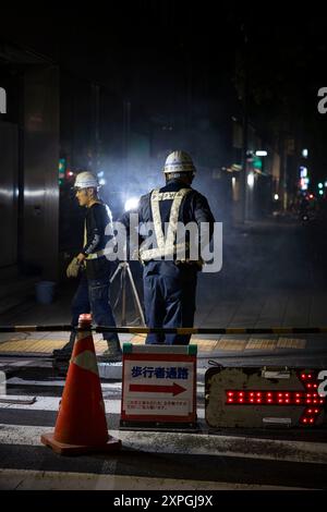 Tokio, Japan. August 2024. Japanische Bauarbeiter bauen nachts eine Straßenbaustelle auf. Neben den farbenfrohen, lebhaften und immer geschäftigen touristischen Hotspots wie Shibuya und Shinjuku bietet Tokio auch ruhigere und authentischere Gegenden, in denen Touristen lokale Küche genießen und echte Erfahrungen mit den Einheimischen machen können. Ein Beispiel für einen solchen Ort ist der alte Tsukiji Fischmarkt in der Nähe von Ginza. (Foto: Stanislav Kogiku/SOPA Images/SIPA USA) Credit: SIPA USA/Alamy Live News Stockfoto