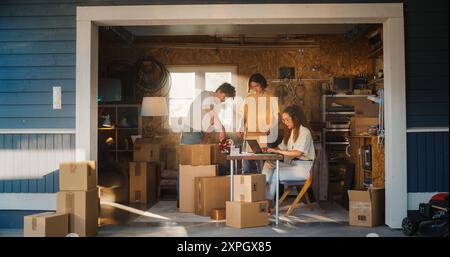 Verschiedene kleine Geschäftspartner, die in der Heimwerkstatt arbeiten. Hispanic Weibliche Managerin, Die Online-Bestellungen Auf Laptop-Computer Ausfüllt. Zwei Kaukasische Männliche Freunde, Die Produkte In Kartons Für Die Lieferung An Kunden Verpacken. Stockfoto