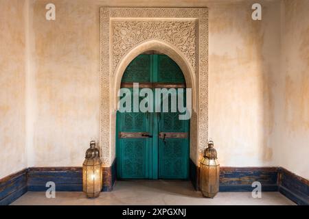 Türkisgrüne blaue marokkanisch verzierte Bogeninnentür, traditionelles geschnitztes dekoratives Holz mit Lampen, Le Jardin Secret, Marrakesch, Marokko. Stockfoto