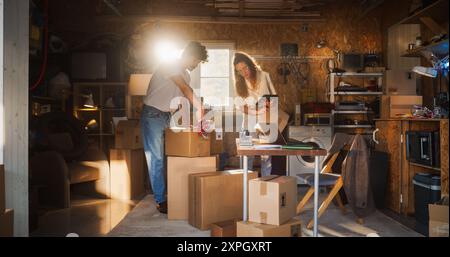 Verschiedene E-Commerce-Geschäftspartner, die in der Werkstatt arbeiten und sich unterhalten. Hispanische Weibliche Assistentin, Die Online-Bestellungen Auf Laptop Ausfüllt. Zwei Kaukasische Freunde, Die Produkte In Kartons Für Die Lieferung An Kunden Verpacken Stockfoto