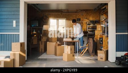 Kaukasischer Geschäftsmann, Der Laptop In Der Garage Benutzt. Männlicher Inhaber Kleiner Unternehmen, Der Bestellungen Von Online-Kunden Ausfüllt. Verpackung Von Produkten In Kartonschachteln Für Den Versand. Unternehmer, Der Zu Hause Arbeitet. Stockfoto