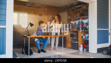 Kaukasischer männlicher Software Engineer und hispanischer weiblicher User Interface Designer sprechen und verwenden Laptop Computer in der Garage zu Hause. Verschiedene Junge Startup-Gründer Arbeiten An Innovativem Online-Service. Stockfoto