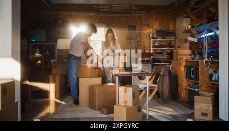 Verschiedene Familienunternehmer arbeiten in der Garage und unterhalten sich. Hispanic Weibliche Managerin, Die Online-Bestellungen Auf Laptop Ausfüllt. Zwei Kaukasische Brüder, Die Produkte In Kartons Für Die Lieferung An Kunden Verpacken. Stockfoto