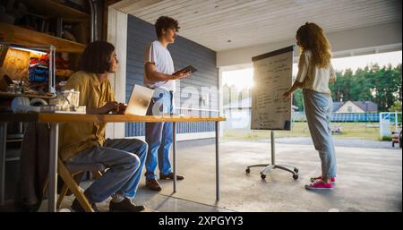 Vielfältiges Team von Jungunternehmern, das Ein Meeting in der Home Garage hält. Hispanic weibliche CEO nutzt Whiteboard, um zwei männliche Kollegen aus Kaukasien mit Laptop und Tablet die Geschäftsziele zu erläutern. Stockfoto