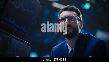 Porträt eines gutaussehenden bärtigen Börsenhändlers, der in einer Börse arbeitet. Erwachsener Mann mit Brille, erforscht Investitionsmöglichkeiten für internationale Unternehmen Stockfoto