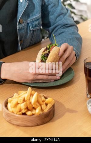 Frau isst leckeren Hamburger mit Pommes frites am Tisch Stockfoto