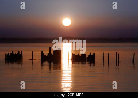 Ein verlassener Steg tauchte teilweise unter wegen Flut mit warmem Ton über dem Wasser vom Sonnenaufgang mit leichtem Nebel in der Ferne Stockfoto