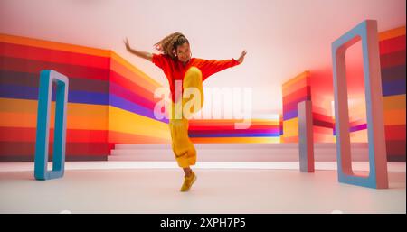 Porträt einer talentierten schwarzen Künstlerin, die energetische Tanzbewegungen in abstrakter farbenfroher Studio-Dekoration zeigt. Afrikanische Frau, die Emotionen mit ihrer innovativen Modern Dance-Routine ausdrückt Stockfoto