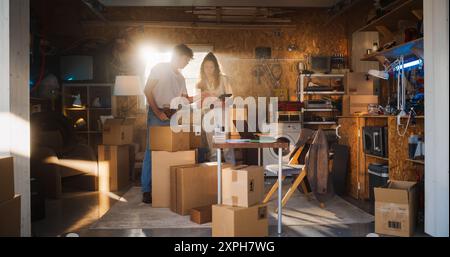 Verschiedene kleine Geschäftspartner, die in der Heimwerkstatt arbeiten und sich unterhalten. Hispanic Weibliche Managerin, Die Online-Bestellungen Auf Laptop Ausfüllt. Zwei Kaukasische Freunde, Die Produkte In Kartons Für Die Lieferung An Kunden Verpacken. Stockfoto