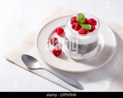 Gesundes und rohes Essen von Kokosjoghurt, Chia Pudding mit frischen Reifen Himbeeren auf einem weißen Teller mit einem Löffel an der Seite Stockfoto