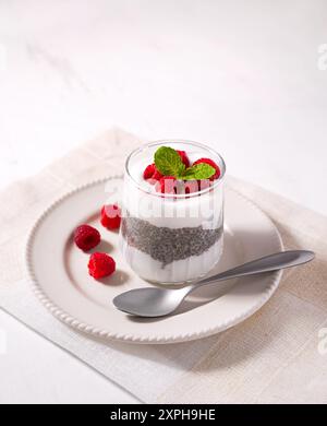 Gesundes und rohes Essen von Kokosjoghurt, Chia Pudding mit frischen Reifen Himbeeren auf einem weißen Teller mit einem Löffel an der Seite Stockfoto