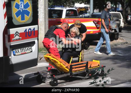 CHARKIW, UKRAINE - 6. AUGUST 2024 - Ein Sanitäter und ein Mann helfen einer verletzten Frau, nach dem russischen Raketenangriff in Charkiw im Nordosten der Ukraine mit einem Krankenwagen auf eine Bahre zu gelangen. Am Dienstagmorgen, dem 6. August, trafen die Russen ein dichtes Wohngebiet im zentralen Teil von Charkow ein. Mindestens fünf Menschen wurden verletzt. Der Charkow-Stadtchef Ihor Terekhov sagte, dass eine Poliklinik, eine der führenden Universitäten der Stadt, ein Schlafsaal und nahe gelegene Gebäude beschädigt worden seien. Stockfoto