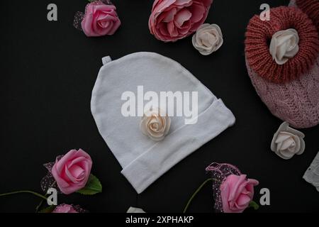 Babykleidung, Schuhe und Rosen auf schwarzem Hintergrund, Babyduschkonzept. Stockfoto