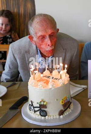 Ein älterer Mann, der den 100. Geburtstag feiert, bläst Kerzen auf seinem Kuchen auf einer Party am 4. August 2024 aus Stockfoto