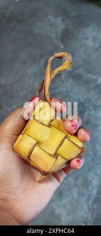 Eine Hand von Frau hielt gekochtes Ketupat oder südostasiatische Reiskuchen-Bündel, oft für Festlichkeiten zubereitet und sehr populäres Gericht während Eid Mubarak cel Stockfoto